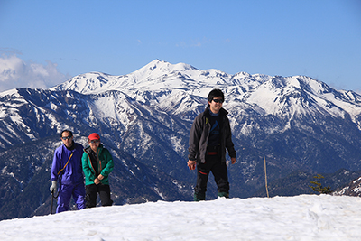 乗鞍岳を背に雪の斜面を登ってきたメンバーの写真
