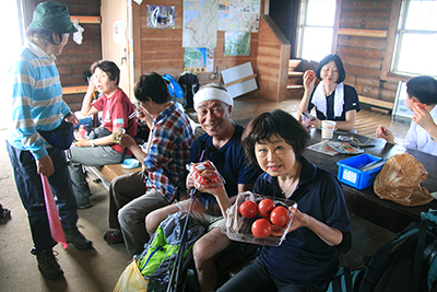 米山山頂の避難小屋で新潟アイユーのＳさんからいただいたトマトとイチゴを持っているＹさんの写真
