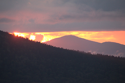 雲の下に姿を現した夕日と森吉山と思われる山の写真