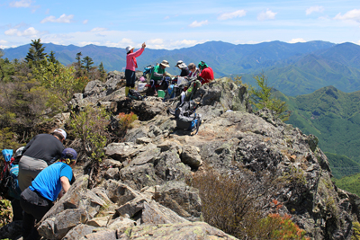山頂部の平らな岩の上で昼食中のメンバーと移動しているメンバーの写真