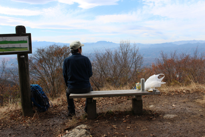 山頂のイスに座って両神山方面を見ているKさんの写真