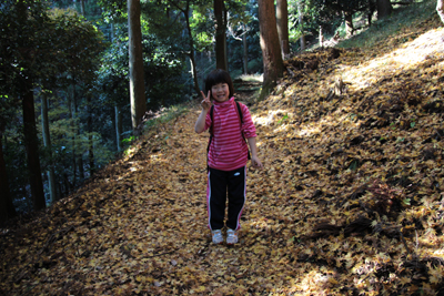 落ち葉の絨毯の上でピースをするＫちゃんの写真