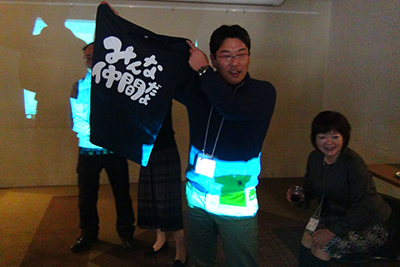 山仲間アルプのＴシャツ案を披露しているＳさんの写真