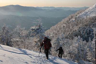 三ツ頭とその下のコルを過ぎて、奥秩父の山々を背に権現岳山頂に向けて登っている写真