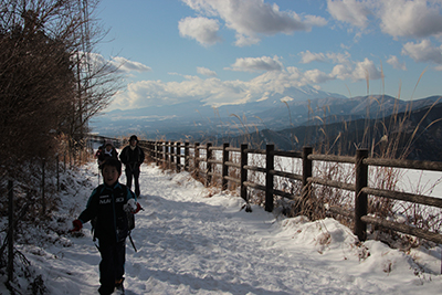 富士山を背に山頂手前の牧場を歩いている写真