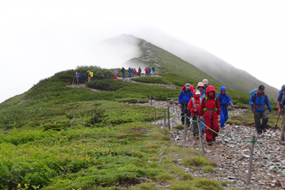 爺ヶ岳を背に種池山荘手前を歩いている写真