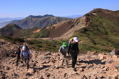 流石山、大倉山を背に朝日岳山頂目指して登っている写真