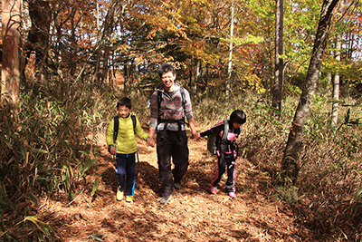 紅葉した登山道を子どもたちと手をつないで歩いているＫさんの写真