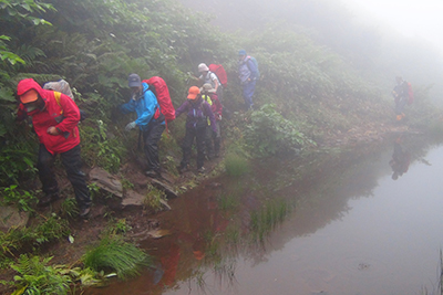 滑ると池に落ちそうな登山道を歩いている写真