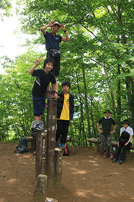 三頭山の山頂標識の上に立つ３人の子どもたちの写真