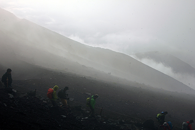 霧が舞い上がる山腹を降りていく人たちの写真