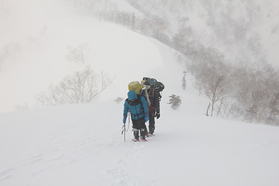 地吹雪の中で小遠見山に登り返している写真