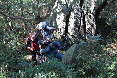 山頂直下の岩のある登山道を登っている写真