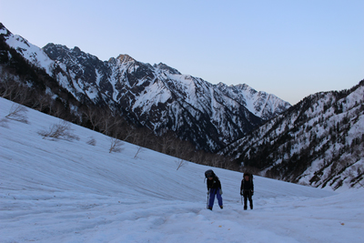 穂高連峰を背に日の出前の残雪斜面を登っている写真