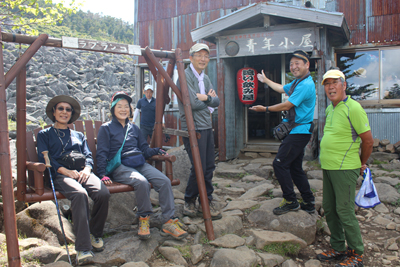 青年小屋の前での集合写真、Iさんが「遠い飲み屋」と書かれた赤提灯を持っているようにポーズを撮っている