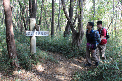 山頂への分岐が書かれた道標を見ているＳさんとＭ君の写真