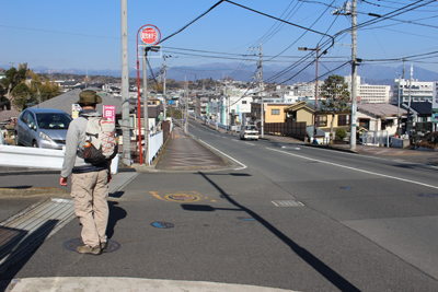 正面に丹沢山地が見える道路にM君が立っている写真