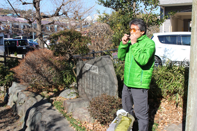 めだかの学校の石碑の横でハーモニカを吹くFさんの写真