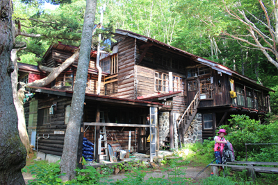 吾妻小屋とその前で出発準備をするFさんの写真