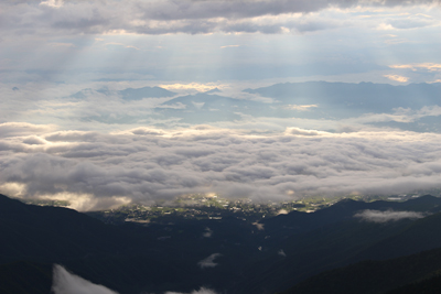 差し込む朝の光と雲海とその下の光る町の写真