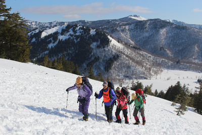 景鶴山を背後に見ながら雪の斜面を登っている写真