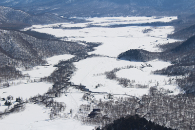 一面の雪原に川が蛇行している尾瀬ヶ原の写真