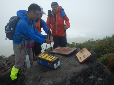 月山山頂で山頂標識に触れている写真